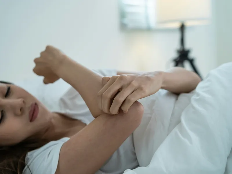 Person experiencing discomfort from insect bites in bed